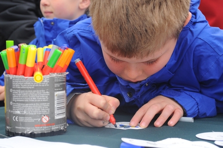 Young boy in a blue raincoat colouring with a felt tip pen.
