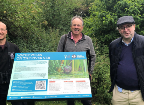 Debs Foundation with Josh Kalms posing for a picture by the River Ver next to an interpretation board about Water Voles