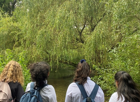 4 schoolgirls wearing rucksacks looking out over a pond in a nature reserve