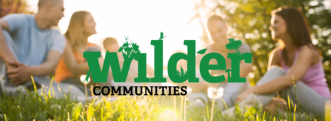 A group of people sitting in a field - Wilder Communities logo superimposed on top