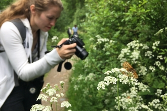 Woman in white jacket taking a photo of green foliage and white flowers