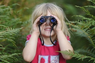 Young girl in red t-shirt looking through binoculars in front of green foliage