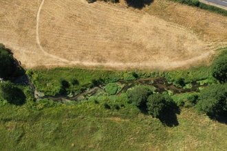 Birdseye view of Archer's Green nature reserve: the river Mimram can be seen horizontally bisecting the photo, in the bottom half is a green meadow, the top half is dry brown grass. The banks of the river are greenest and there are trees dotted along its length.