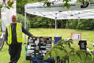 A man in a reflective jacket is standing in a gazebo by a pin board with pictures and text about the local river on it.