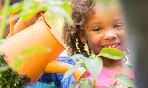 Girl smiling while using watering can to water a small plant