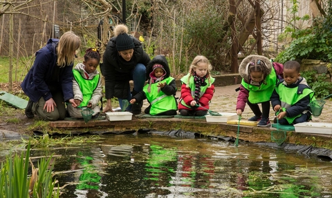 Children in reflective green jackets accompanied by adults pond dipping