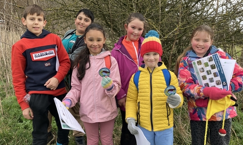 A group of children smiling at the camera holding up Chalk Stream Challenge badges and worksheets