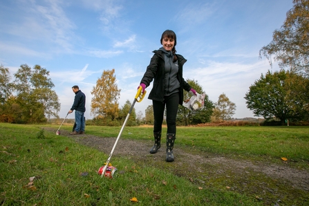 Woman picking up litter with a stick in a park