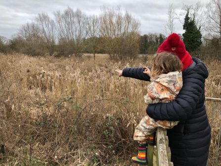 Woman holding child and pointing at trees and grassland in early spring