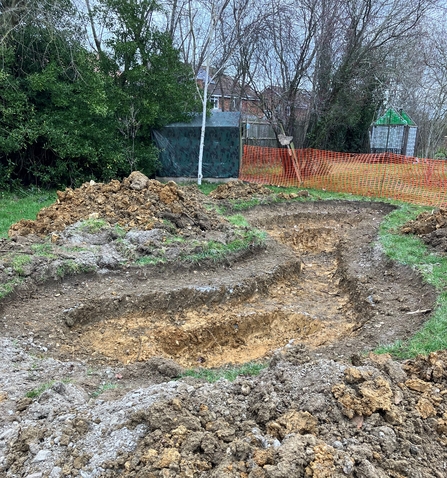 Pond shape dug out of the muddy ground with trees and shed in the background