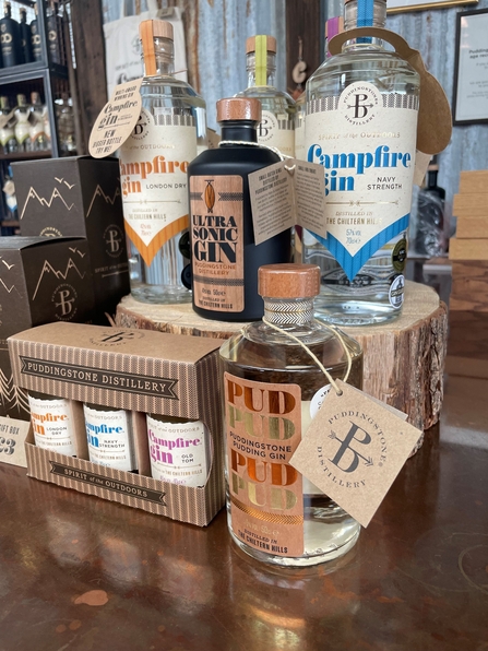 A selection of bottles of Puddingstone Distillery's Gin. In the centre is a black bottle of Ultrasonic Gin labelled in warm brown. 