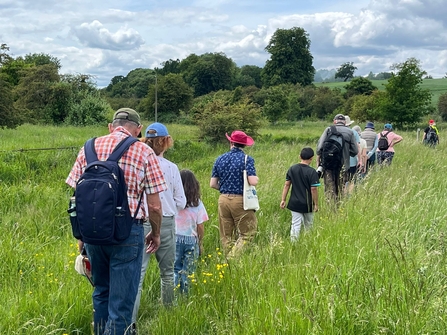 Adults and children walking through long grass at Kings Meads Nature Reserve on a guided walk