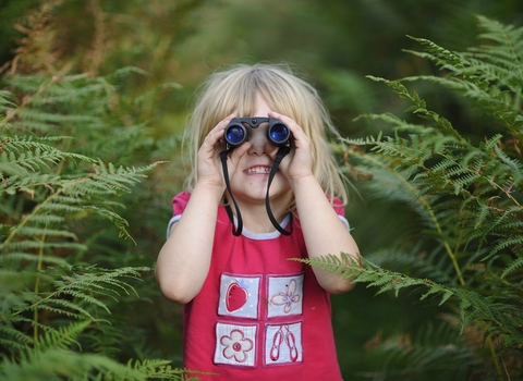Young girl in a red t-shirt bird watching with ferns in the background.